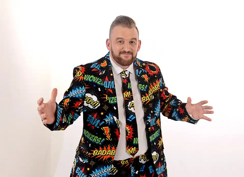 Man in colorful comic-themed suit with open arms against white background.