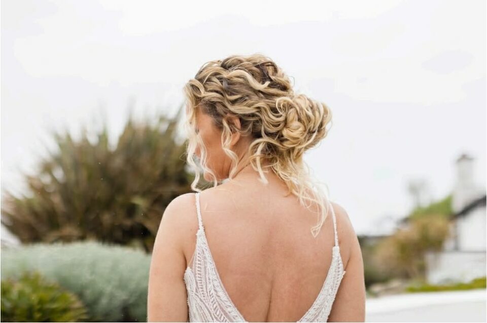 Woman with curly updo hairstyle in sleeveless dress, outdoor setting.
