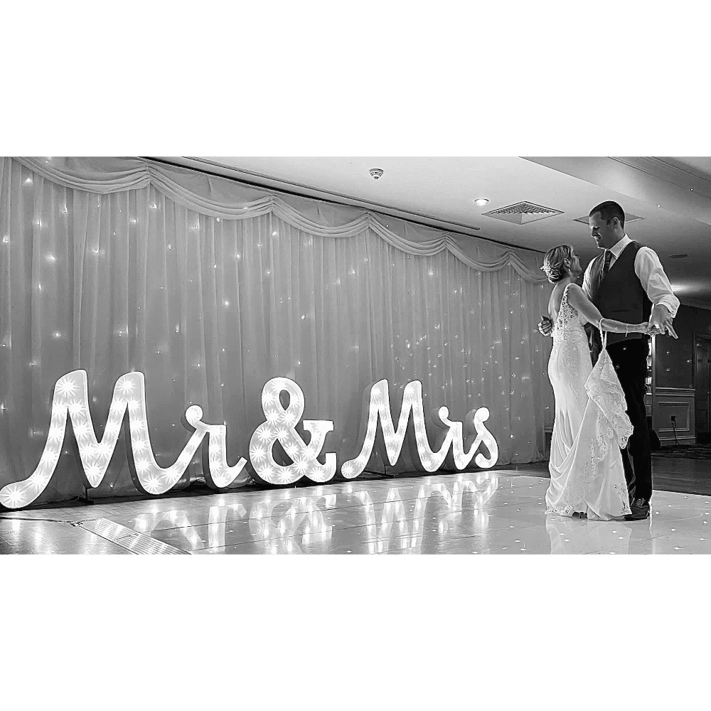 Bride and groom dancing near illuminated "Mr & Mrs" sign at a wedding reception.