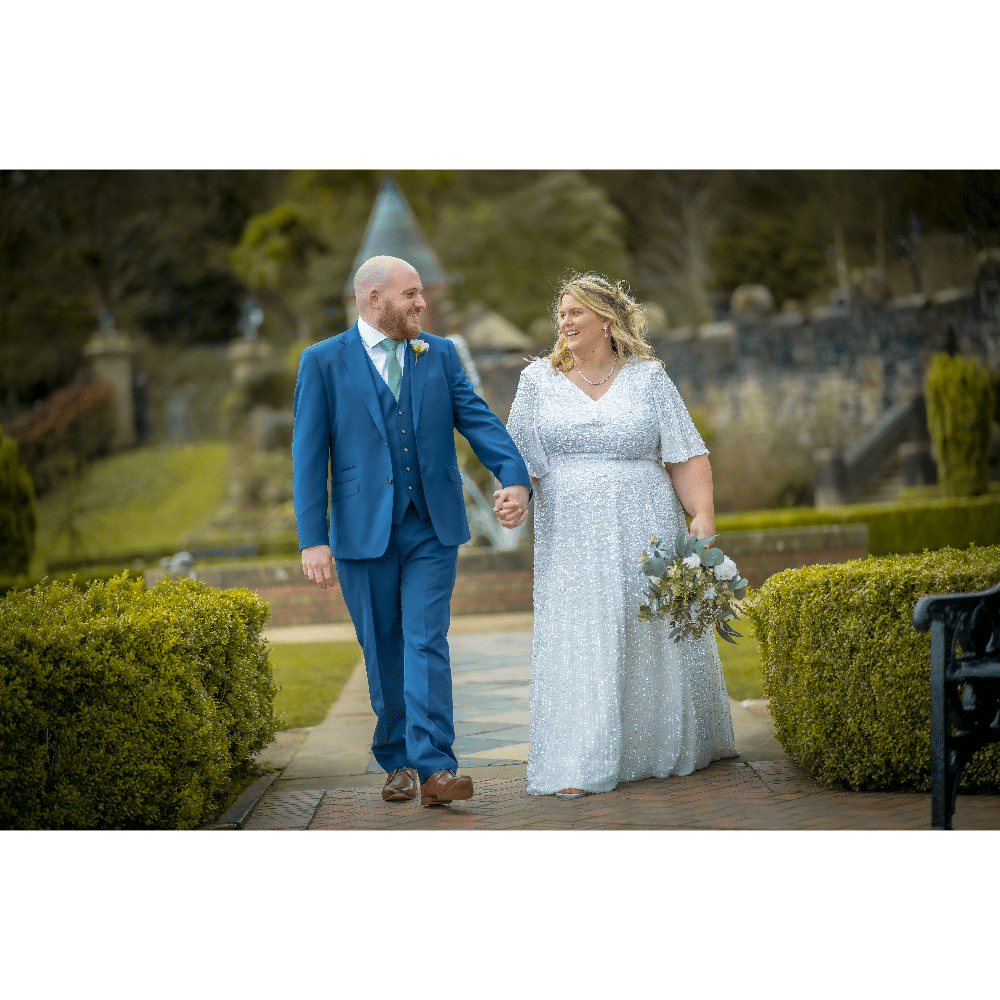 Bride and groom walking hand in hand in a garden setting.