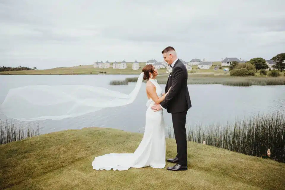 Wedding couple by lakeside with veil flowing, featured in vendor listing card.