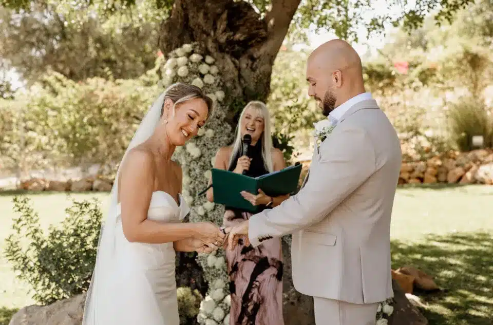 Outdoor wedding ceremony with celebrant officiating couple under a tree, featured in vendor listing card.