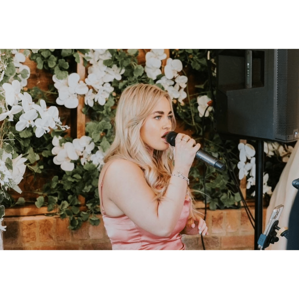 Woman singing into a microphone with floral background.