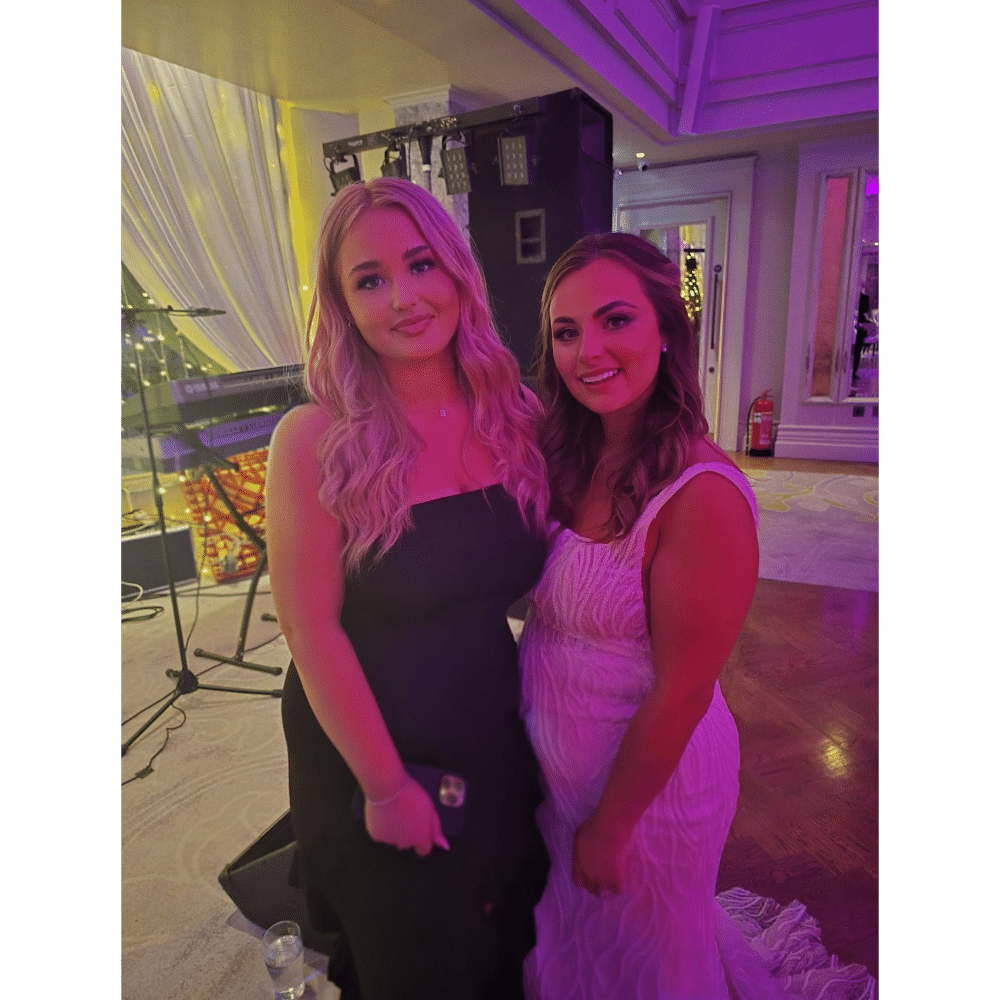 Two women posing at an indoor event with purple lighting.
