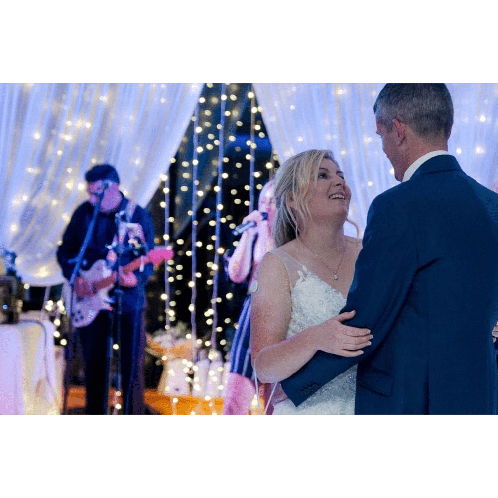 Bride and groom dancing at wedding reception with live band in background.