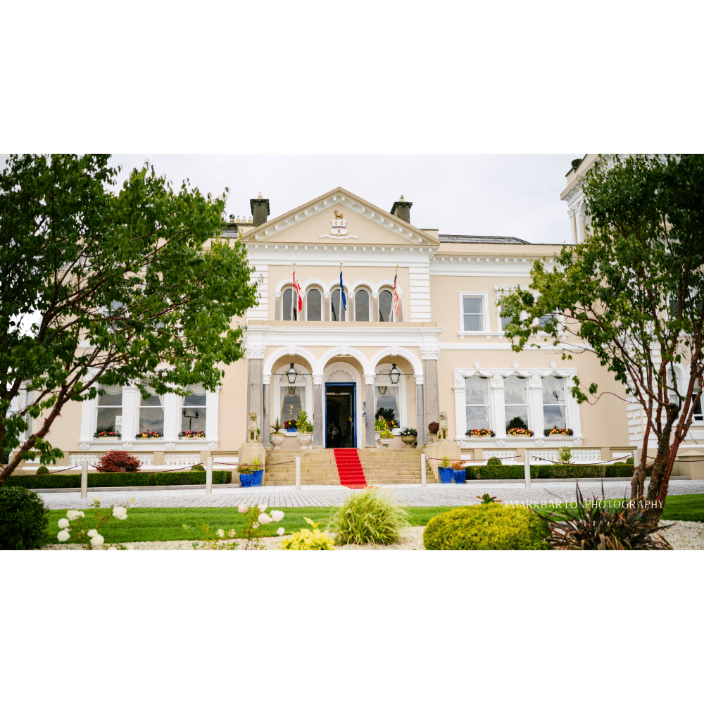 Elegant mansion with red carpet entrance, surrounded by greenery and adorned with international flags.