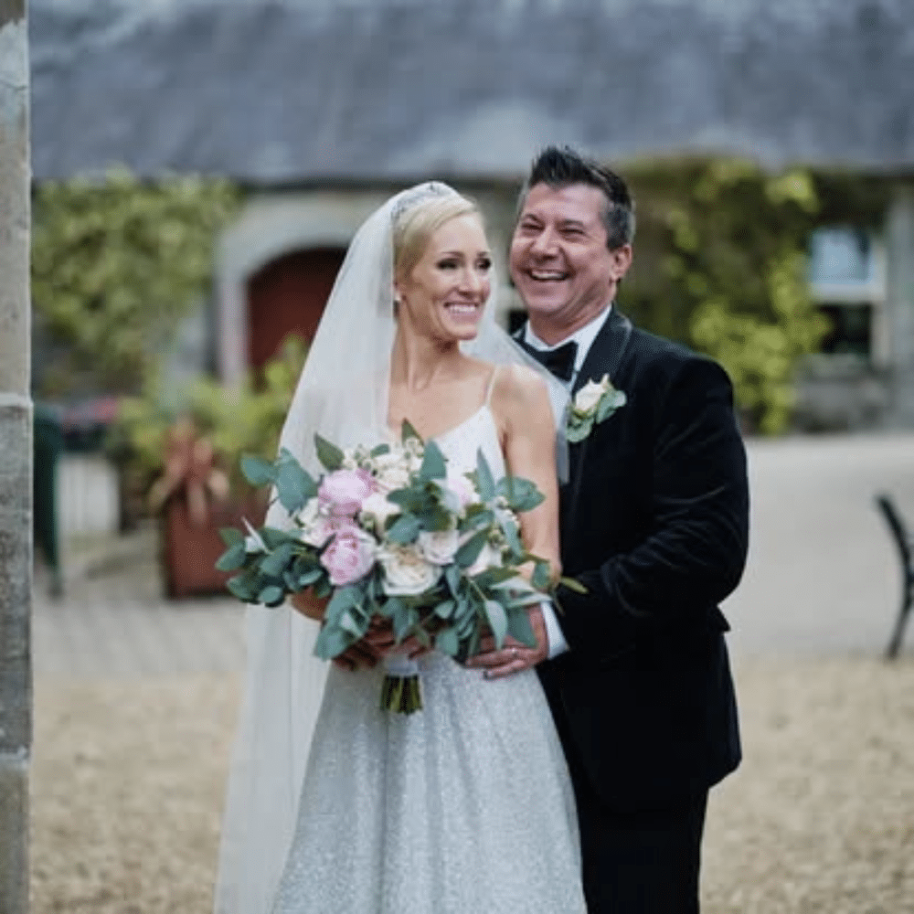 Bride and groom smiling and embracing outdoors in wedding attire.