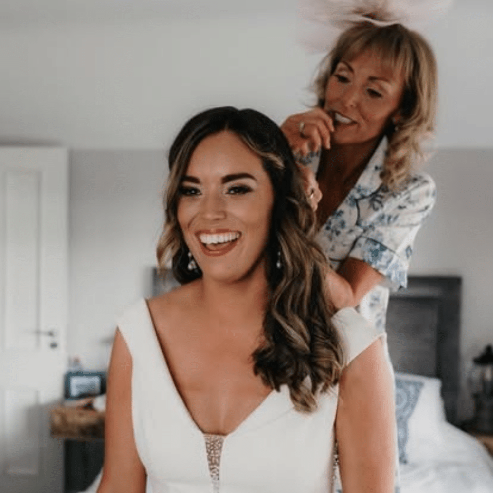 Bride getting ready with help, smiling in a bedroom.