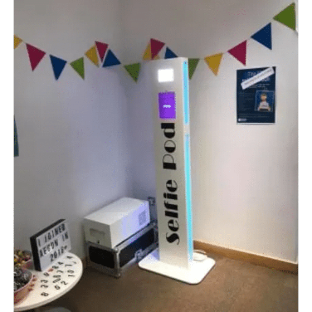 Selfie pod in a decorated room with colorful bunting and a lightbox sign.
