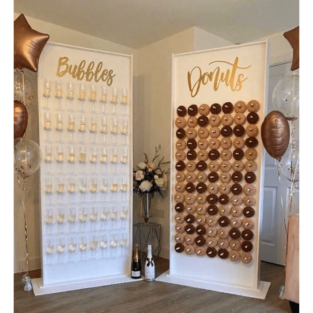 Champagne and donut display with balloons, featuring prosecco glasses and assorted donuts on stands, event decor.