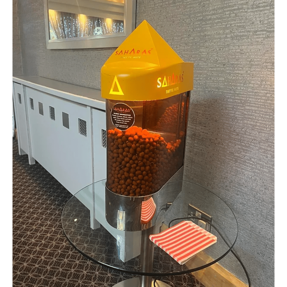 Saharas nuts dispenser on a glass table with striped napkins nearby in a room setting.