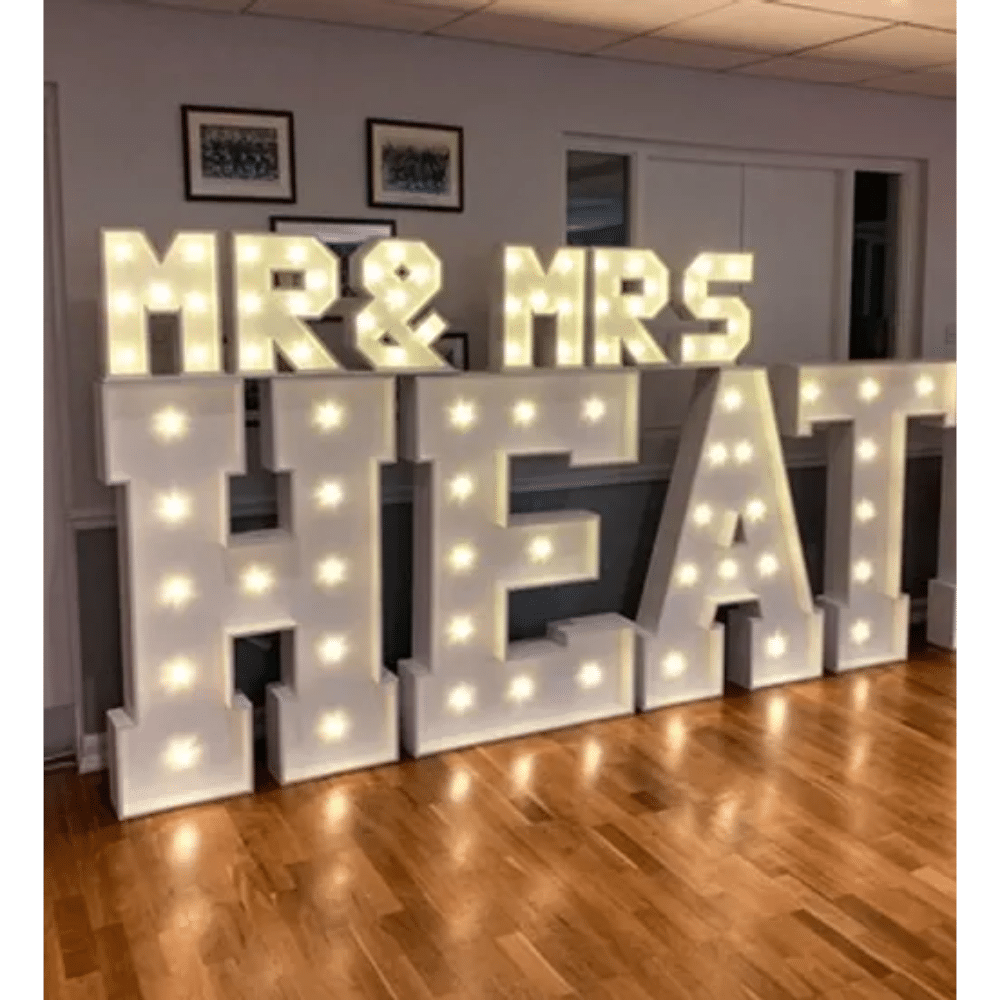 Illuminated "Mr & Mrs HEAT" sign on wooden floor in a decorated room.