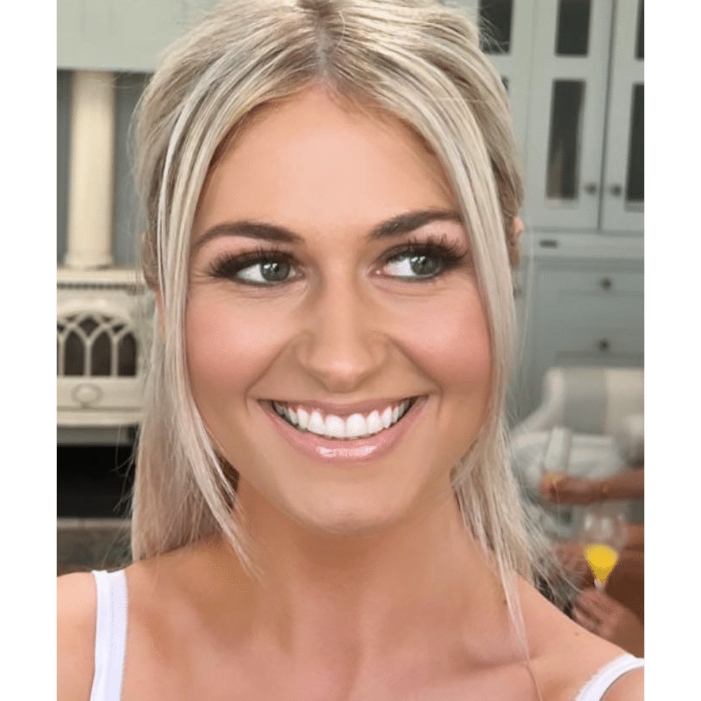 Smiling woman with blonde hair and bright eyes, standing indoors.