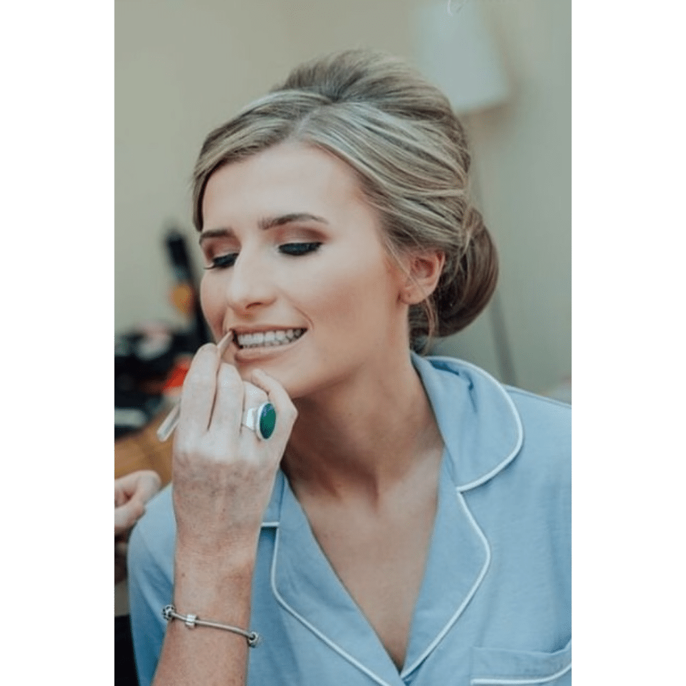 Woman in blue pajamas having makeup applied, smiling.
