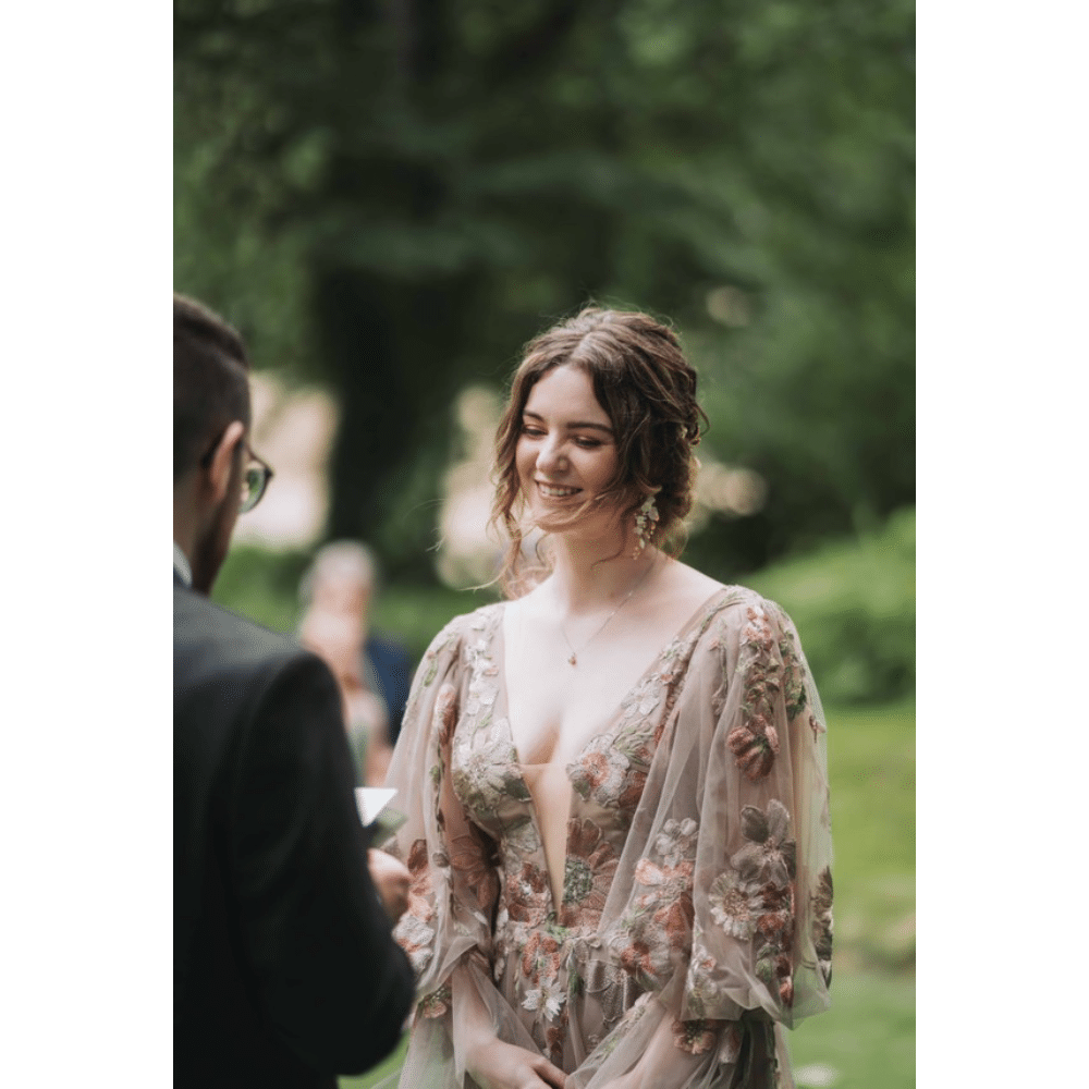 Woman in floral dress smiles during outdoor ceremony with blurred background.