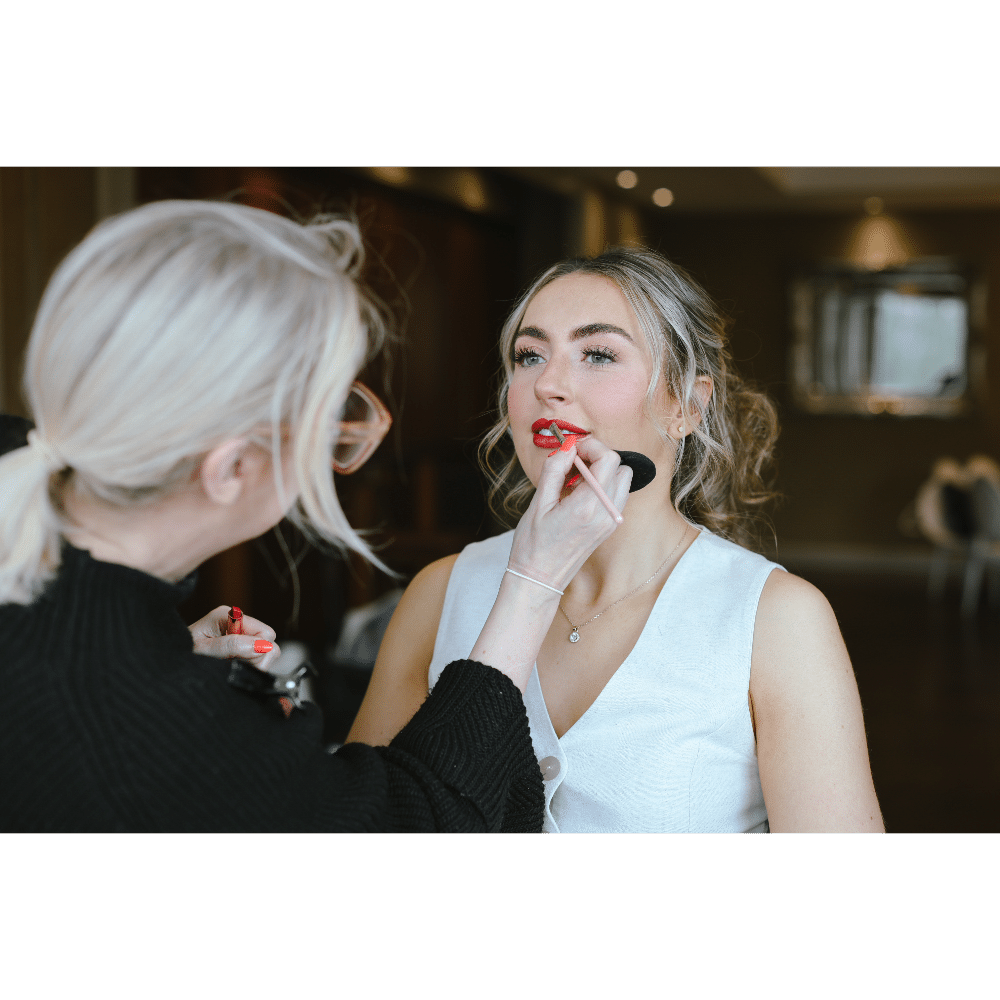Makeup artist applying lipstick and foundation to a woman.