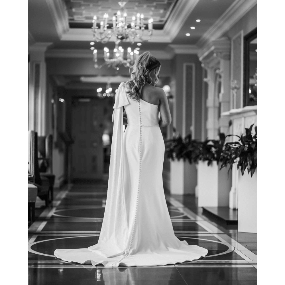 Bride in an elegant white gown walking down a corridor with chandeliers.