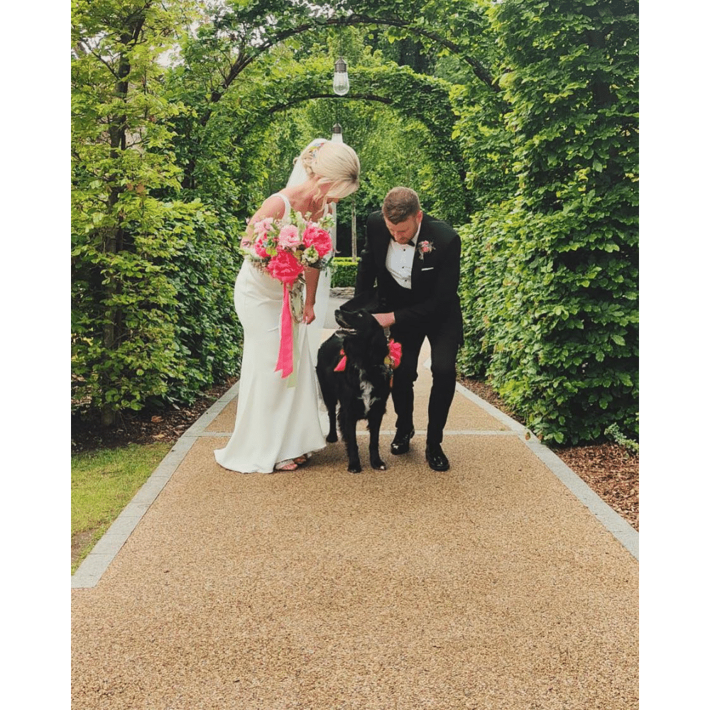 Bride and groom with a black dog under a green archway.