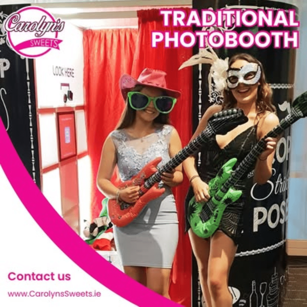Two women posing with inflatable guitars and wearing costumes in a traditional photobooth setting at Carolyn's Sweets event.