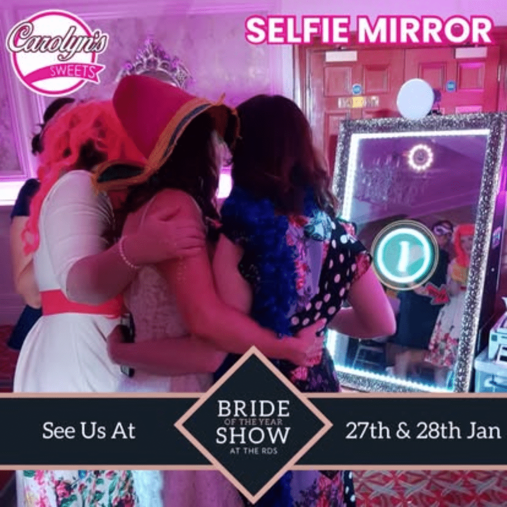 Group of people taking a selfie in front of a mirror at a bridal show, with colorful lighting and decorative signage.
