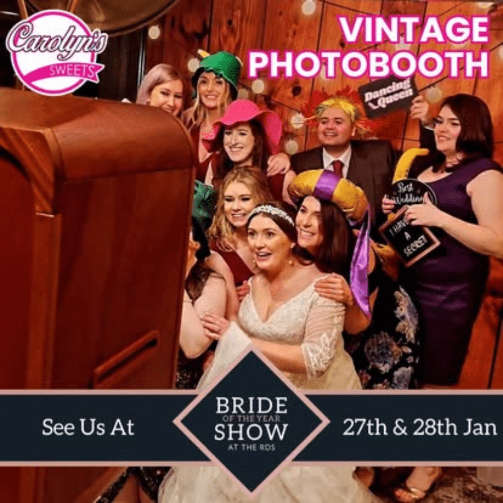 Group taking a fun photo in a vintage photobooth at a bridal event, wearing colorful hats and props.