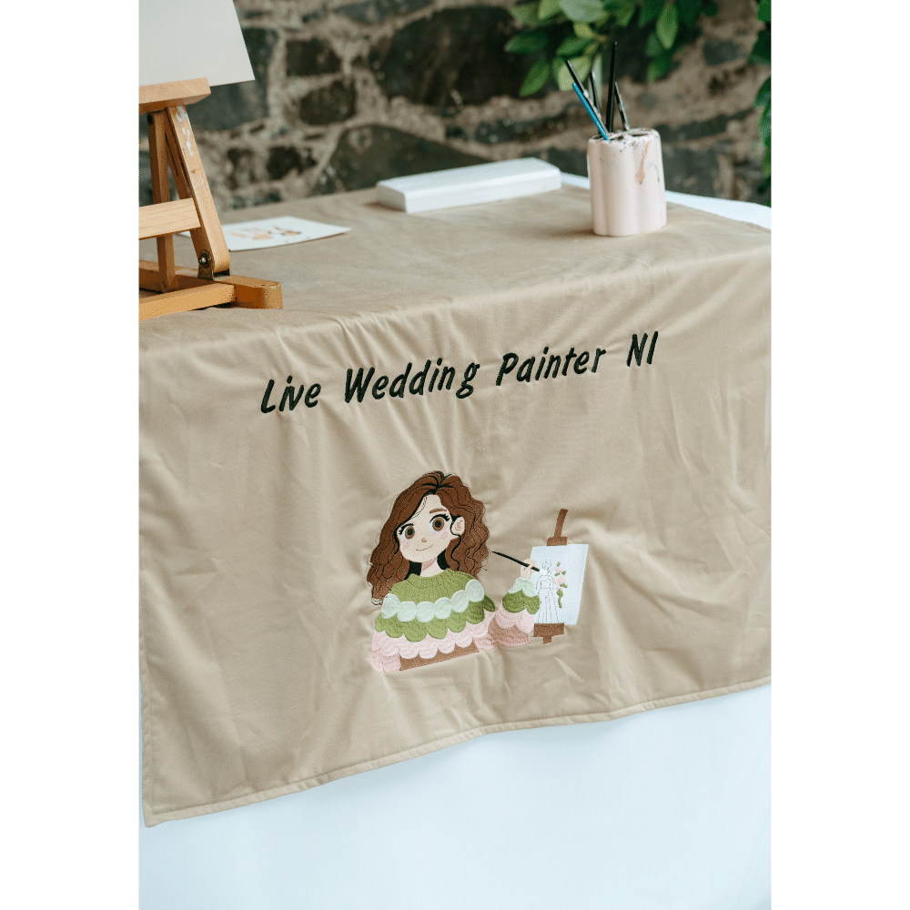 "Table with beige cloth featuring 'Live Wedding Painter NI' and a cartoon artist illustration."