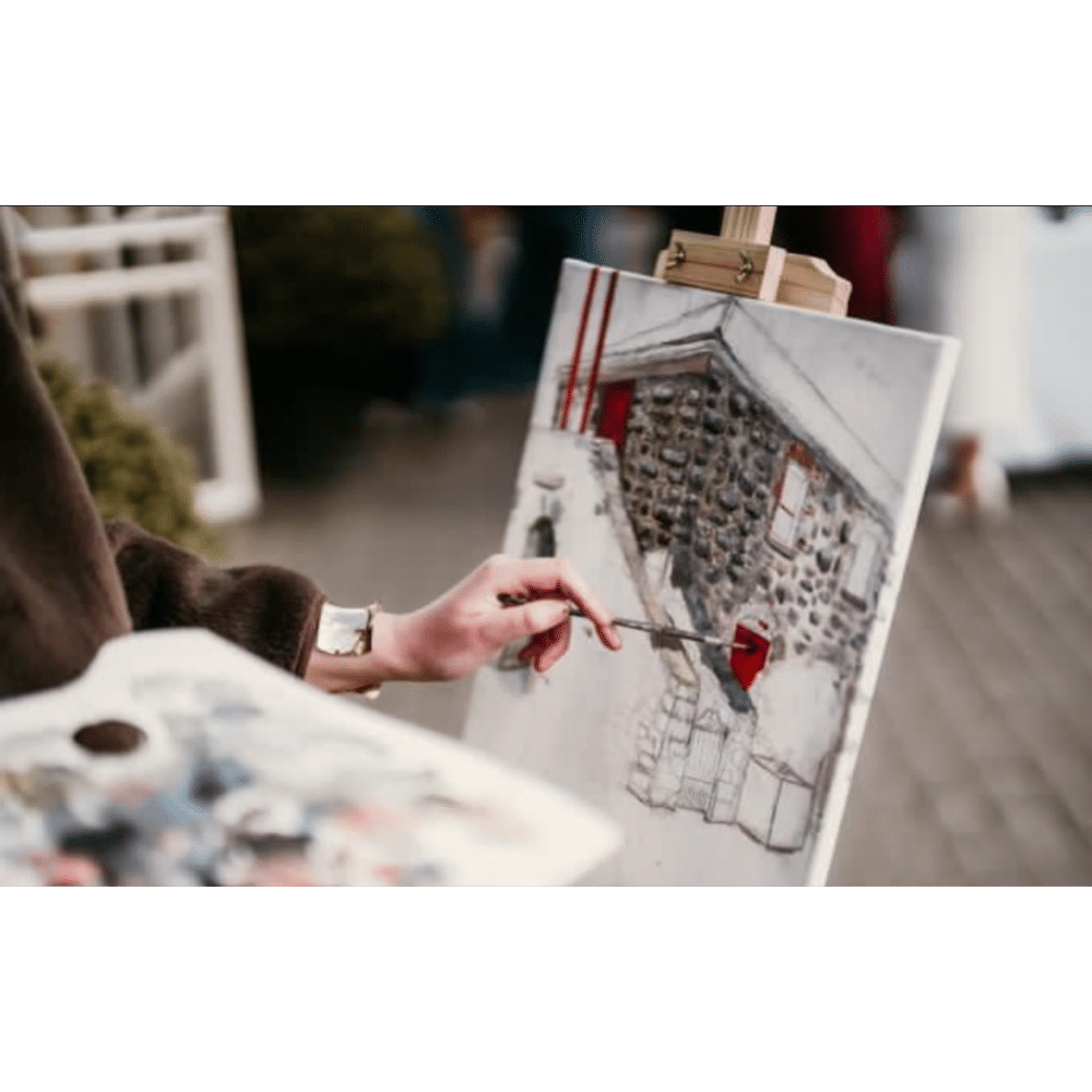 Artist painting a stone house on a canvas outdoors, holding a palette.