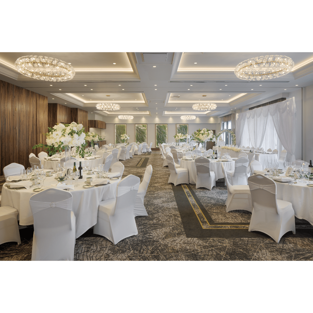 Elegant wedding reception hall with white tablecloths, floral centerpieces, and chandeliers.