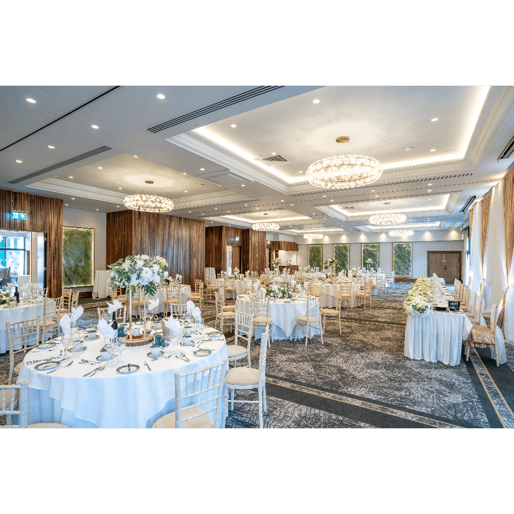 Elegant wedding reception setup with round tables, floral centerpieces, and ornate chandeliers in a spacious ballroom.