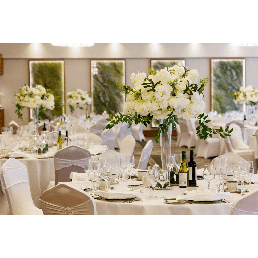 Elegant wedding reception with round tables, white floral centerpieces, wine bottles, and white chair covers.