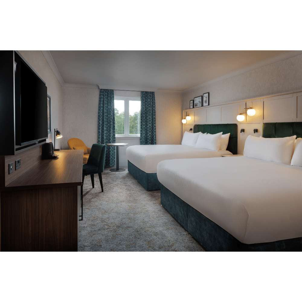 Modern hotel room with two double beds, a large window, a desk with a TV, and stylish lighting fixtures.
