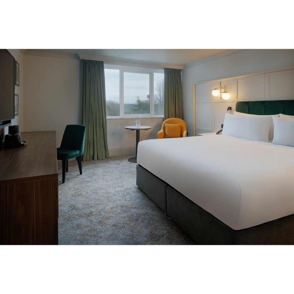 Modern hotel room with double bed, green chair, desk, and window view.