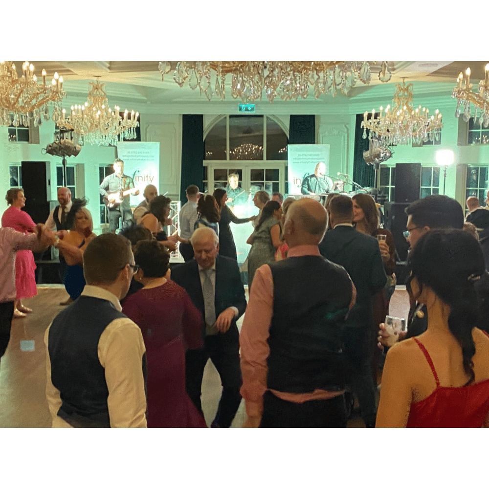 People dancing in a ballroom with chandeliers and live musicians performing on stage.
