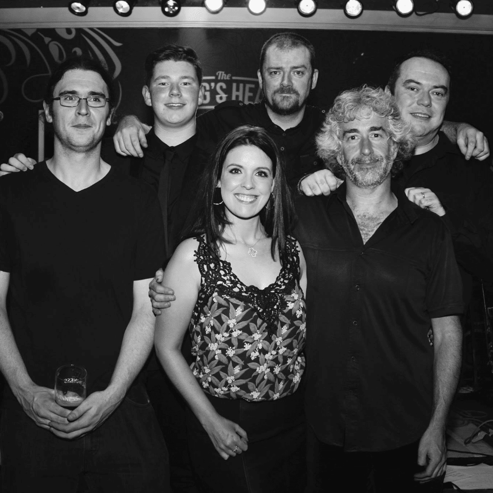 Group of six people smiling, posing together at the King's Head venue, black and white photo.