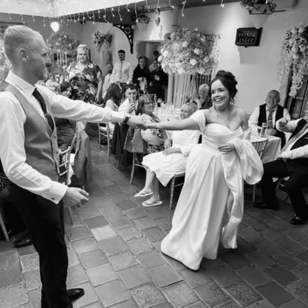Bride and groom dancing at a wedding reception, guests seated in the background.