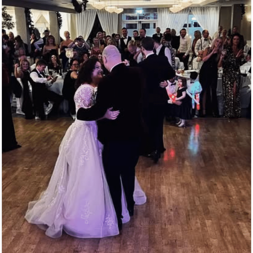 Bride and groom dancing at a wedding reception with guests watching.