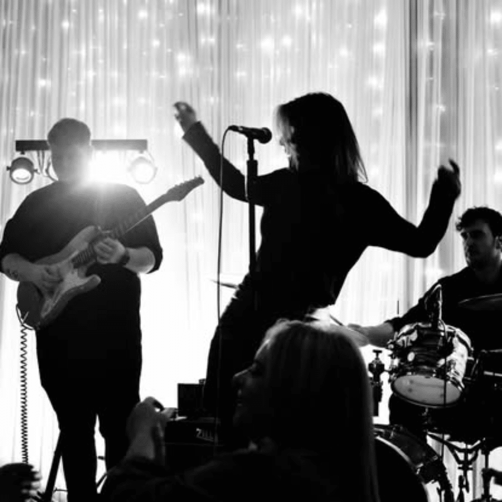 Silhouetted band performing on stage with guitar, drums, and singer. Backdrop of fairy lights.