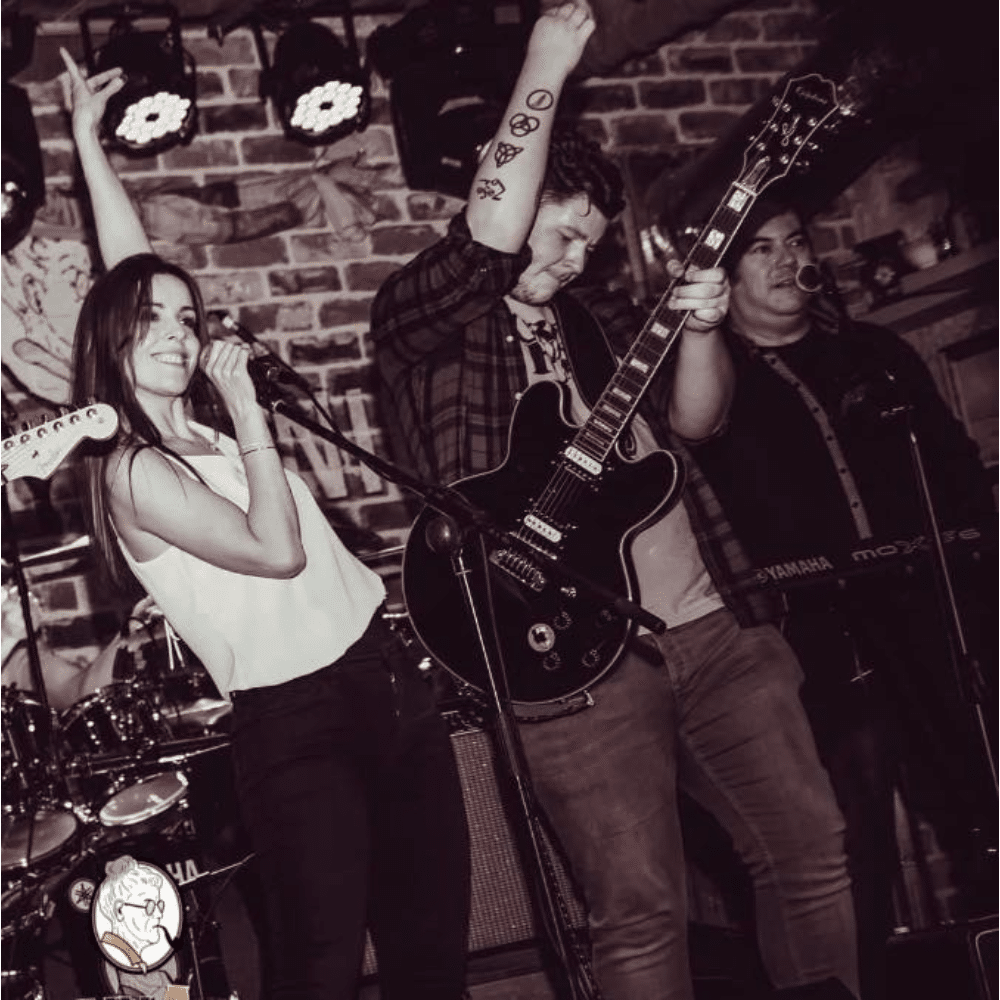 Band performing on stage with a singer, guitarist, and keyboard player in a lively atmosphere.
