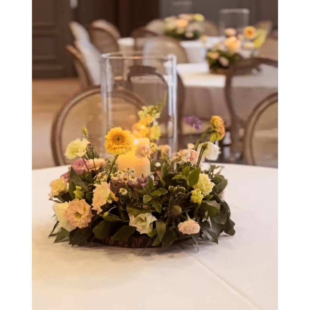 Floral centerpiece with candle in glass holder on a table.