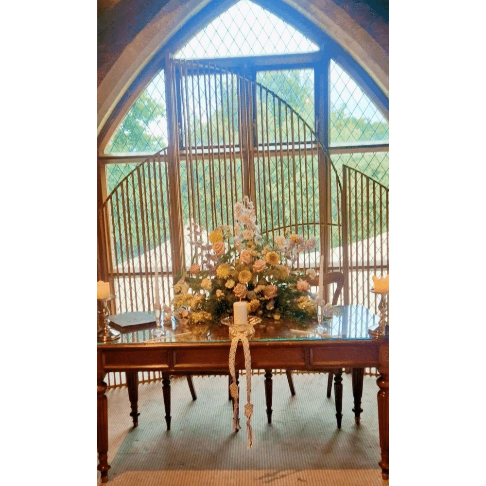 Elegant wedding altar setup with floral arrangement, candles, and an arched window background.