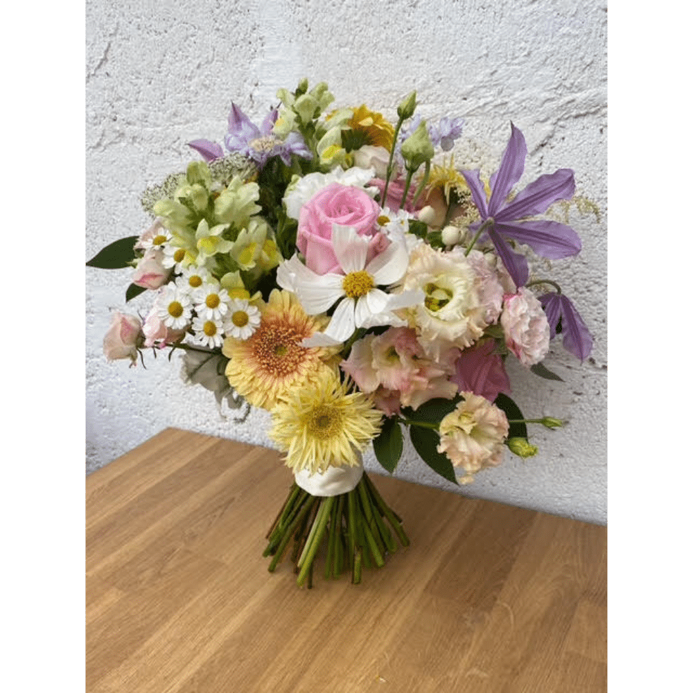 Bouquet of assorted flowers with pink roses, daisies, and purple blooms on a wooden table.