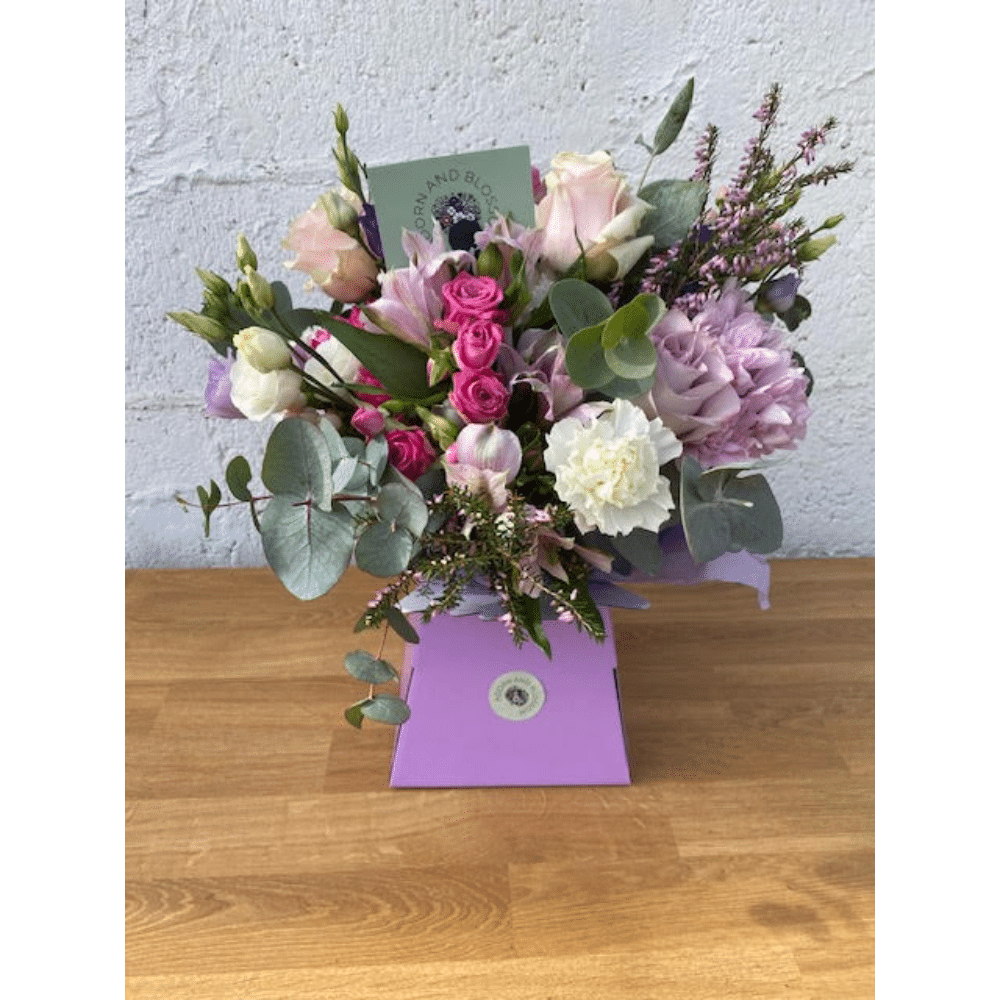 Floral arrangement with pink, white, and purple blooms in a purple box on a wooden surface.