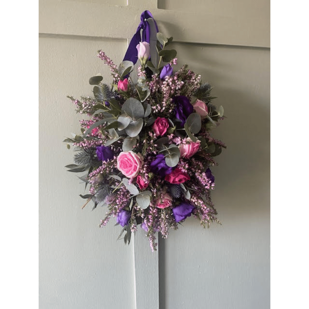 Floral arrangement with pink roses, purple flowers, and eucalyptus hanging on a door.