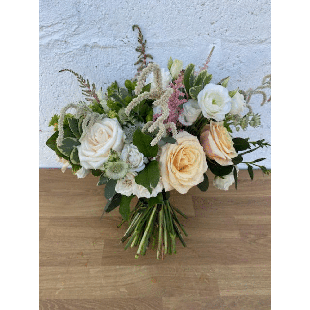 A bouquet of mixed flowers with white and peach roses on a wooden surface.