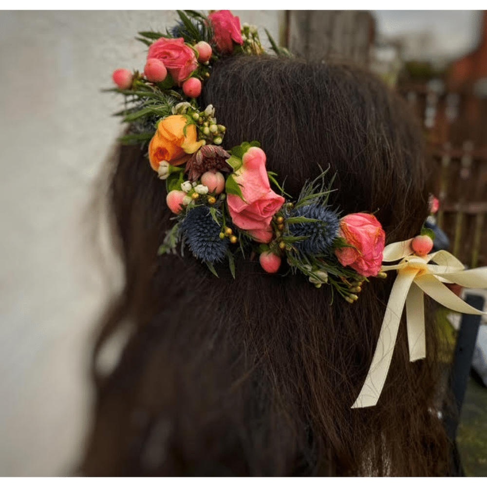 Floral headpiece with pink, orange roses, thistle, and berries on dark brown hair.