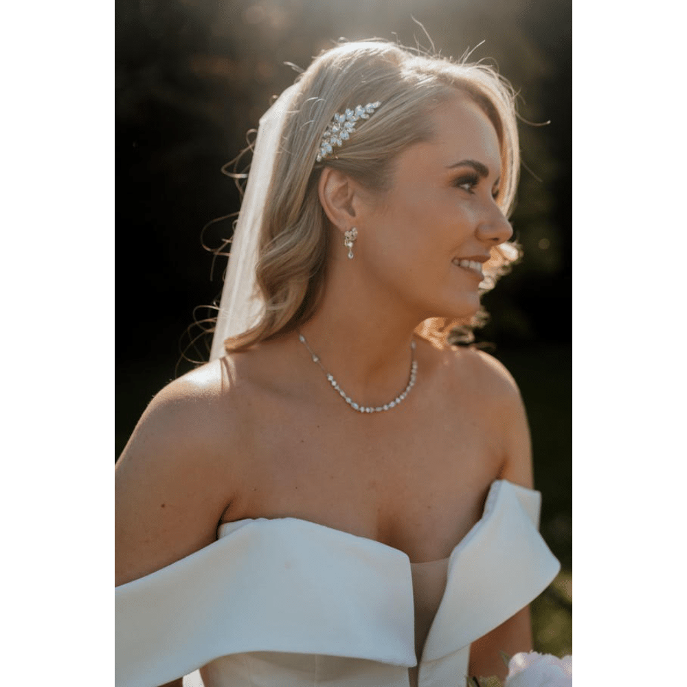 Smiling bride with pearl necklace and hair accessories in sunlight.