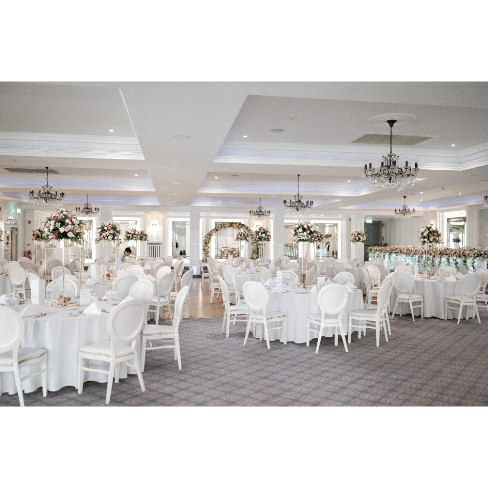 Elegant wedding reception hall with round tables, white chairs, and floral centerpieces.