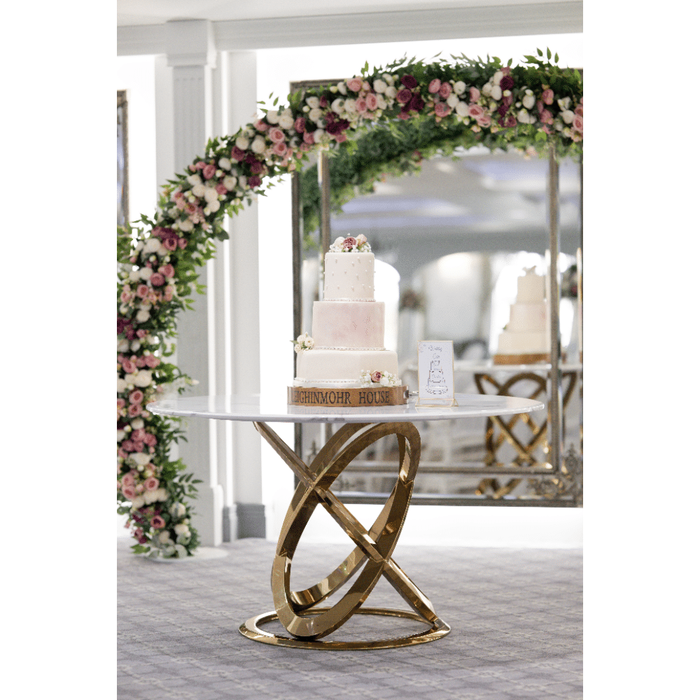 Elegant wedding cake on a marble table with floral arch backdrop.