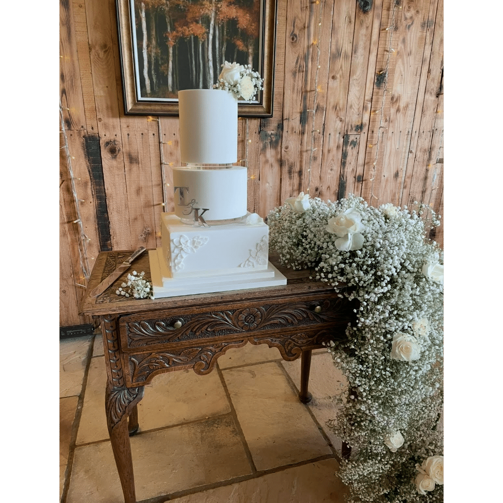 Elegant white wedding cake on a carved wooden table with floral decorations.