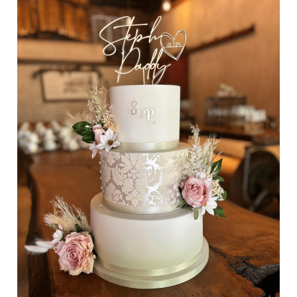 Elegant three-tiered wedding cake with floral decorations and personalized topper on a wooden table.